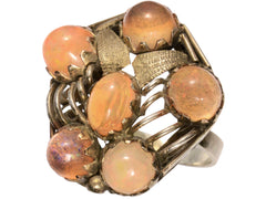 thumbnail of Right angled view of pentagonal Arts & Crafts movement ring with six fire opal cabochons set in a filigreed mounting, shown on white background.