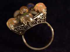 thumbnail of Angled profile view of pentagonal Arts & Crafts movement ring with six fire opal cabochons set in a filigreed mounting, shown on dark background.