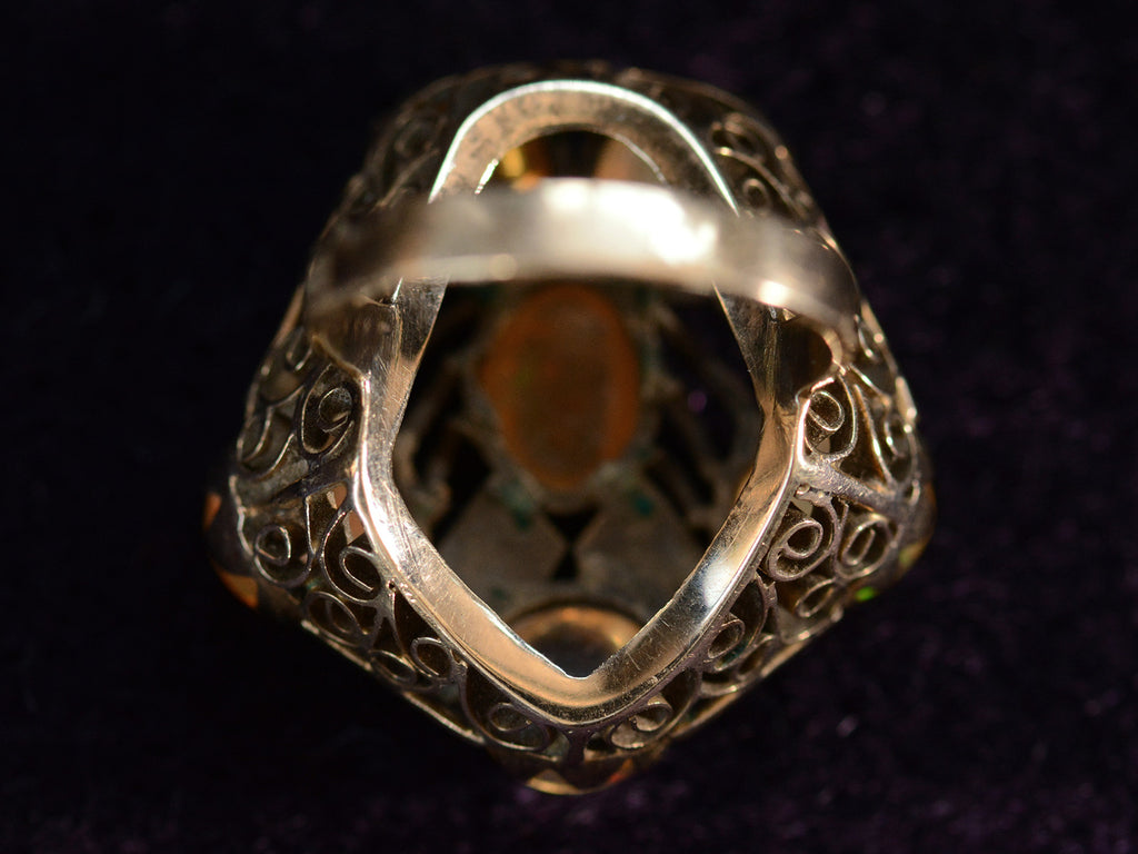 Reverse view of inside pentagonal Arts & Crafts movement ring with six fire opal cabochons set in a filigreed mounting, shown on dark background.