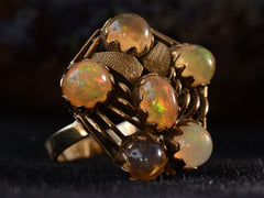 thumbnail of Left angled view of pentagonal Arts & Crafts movement ring with six fire opal cabochons set in a filigreed mounting, shown on dark background.