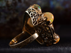 thumbnail of Side detail view of pentagonal Arts & Crafts movement ring with six fire opal cabochons set in a filigreed mounting, shown on dark background.