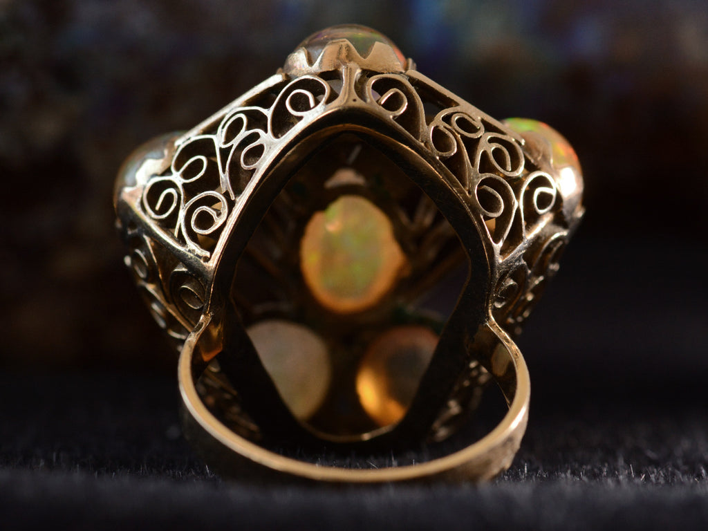Reverse detail view of pentagonal Arts & Crafts movement ring with six fire opal cabochons set in a filigreed mounting, shown on dark background.