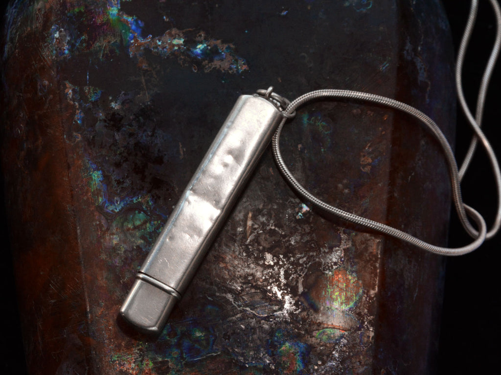 Reverse side of silver pendant with fish decoration, showing dents, on dark background.