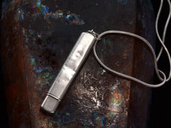 thumbnail of Reverse side of silver pendant with fish decoration, showing dents, on dark background.