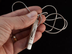 thumbnail of Detail of silver pendant with fish decoration, shown held in hand.