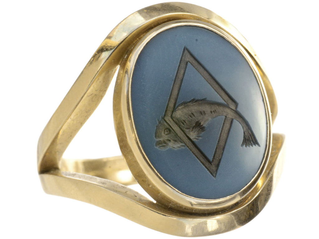 A vintage French yellow gold signet ring with the image of a fish jumping through a lozenge shape carved into blue and black chalcedony. Shown on white background.