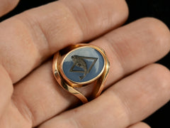 thumbnail of A vintage French yellow gold signet ring with the image of a fish jumping through a lozenge shape carved into blue and black chalcedony. Shown on hand.
