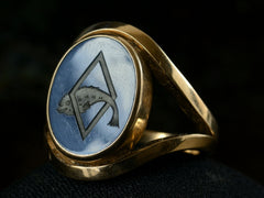 thumbnail of Right angled front view of a vintage French yellow gold signet ring with the image of a fish jumping through a lozenge shape carved into blue and black chalcedony. Shown on dark background.