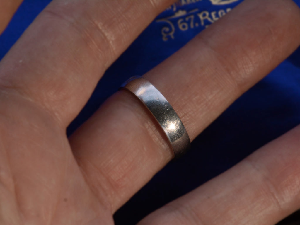 A vintage c1980 flat men's wedding band in platinum, shown on a finger for scale.