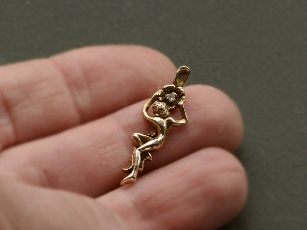 Gold vintage pendant in the form of a a woman hanging from a flower (shown on hand)