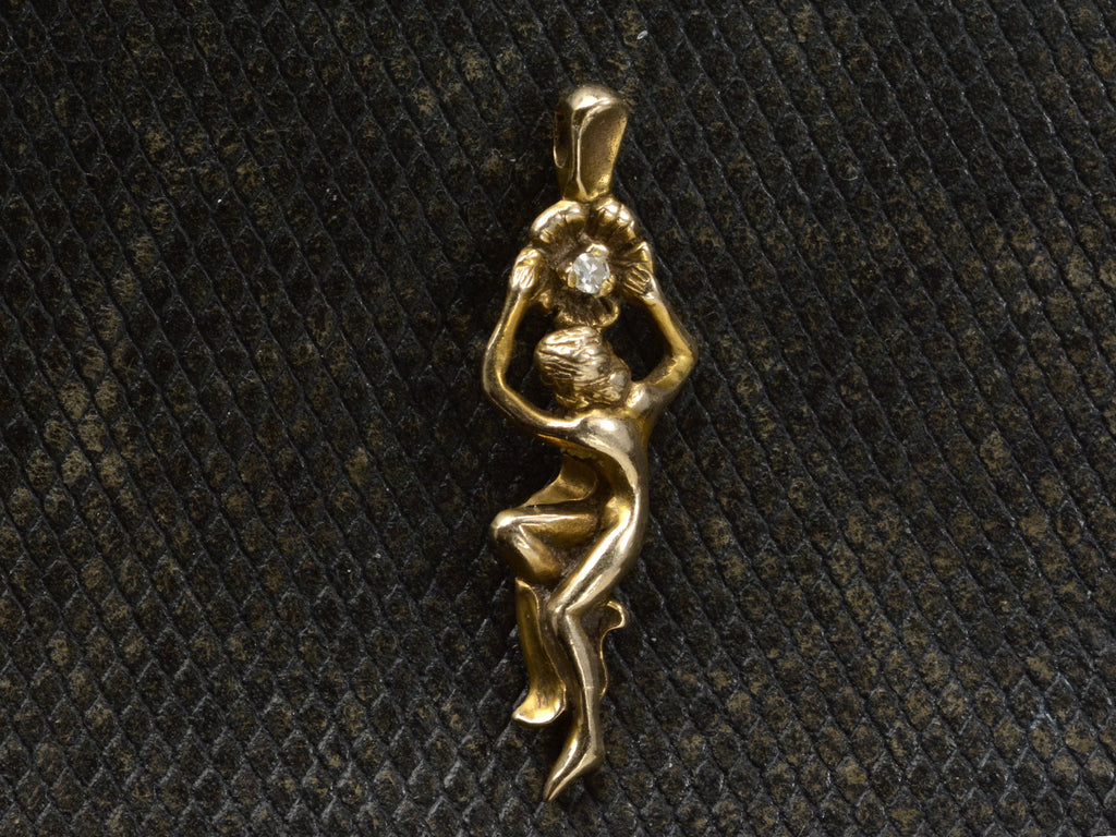 Gold vintage pendant in the form of a a woman hanging from a flower (shown on dark textured background)