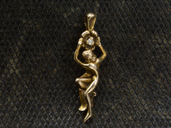 thumbnail of Gold vintage pendant in the form of a a woman hanging from a flower (shown on dark textured background)