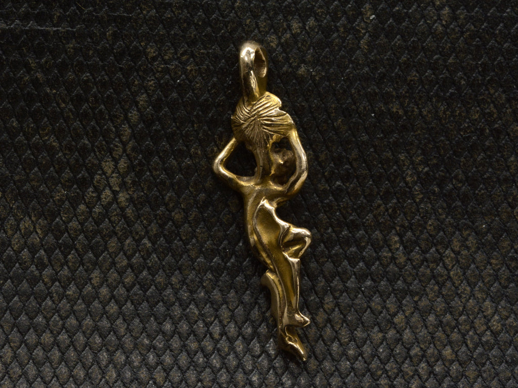 Reverse side of vintage pendant in the form of a a woman hanging from a flower (shown on dark textured background)
