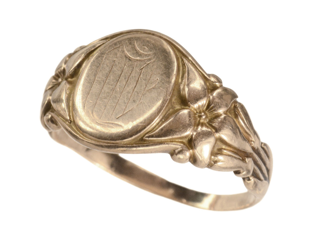 Angled view of antique rose gold Art Nouveau signet ring with lily designs, shown on white background. 