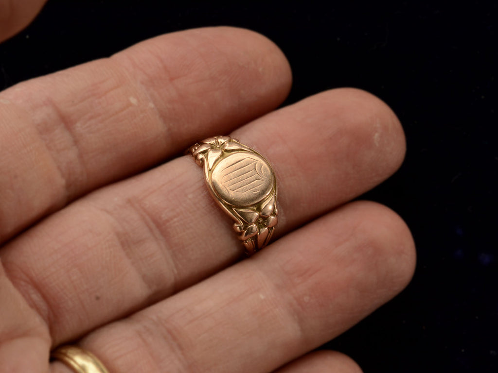 Front view of antique rose gold Art Nouveau signet ring with lily designs, shown on finger