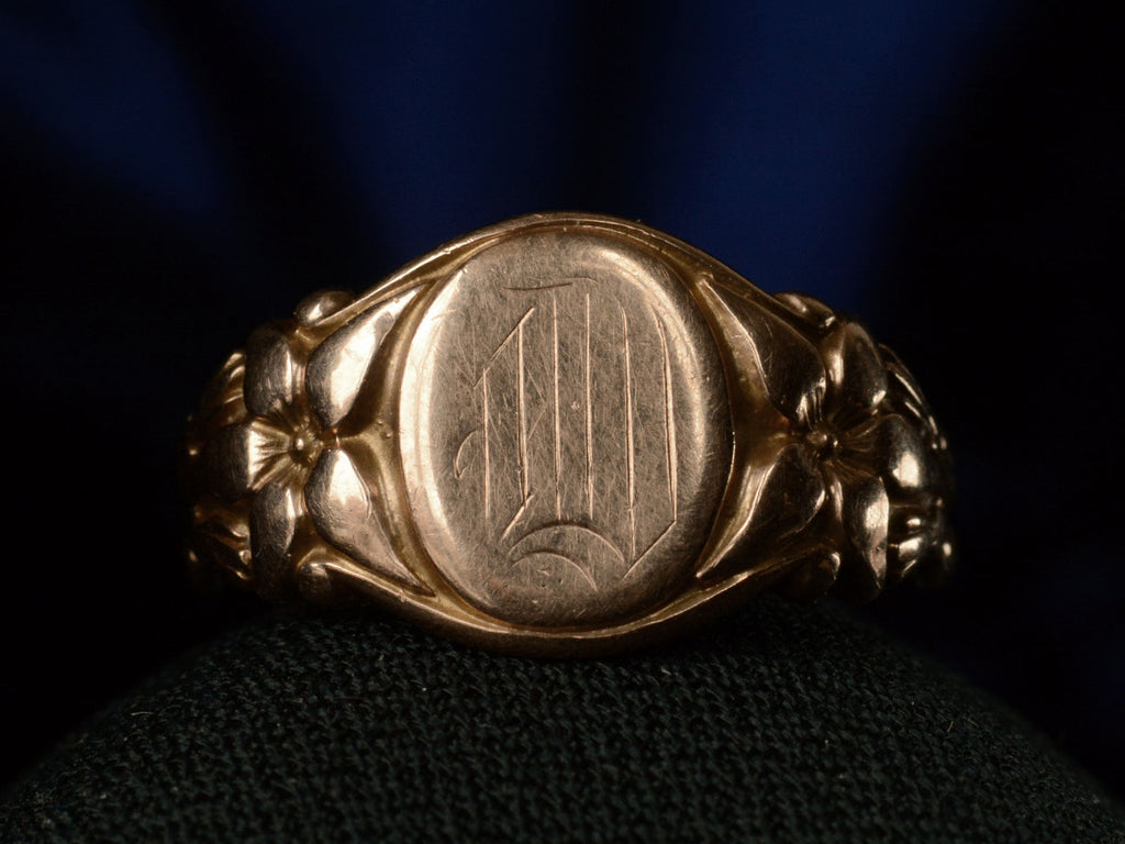 Front view of antique rose gold Art Nouveau signet ring with lily designs, shown on dark background. 