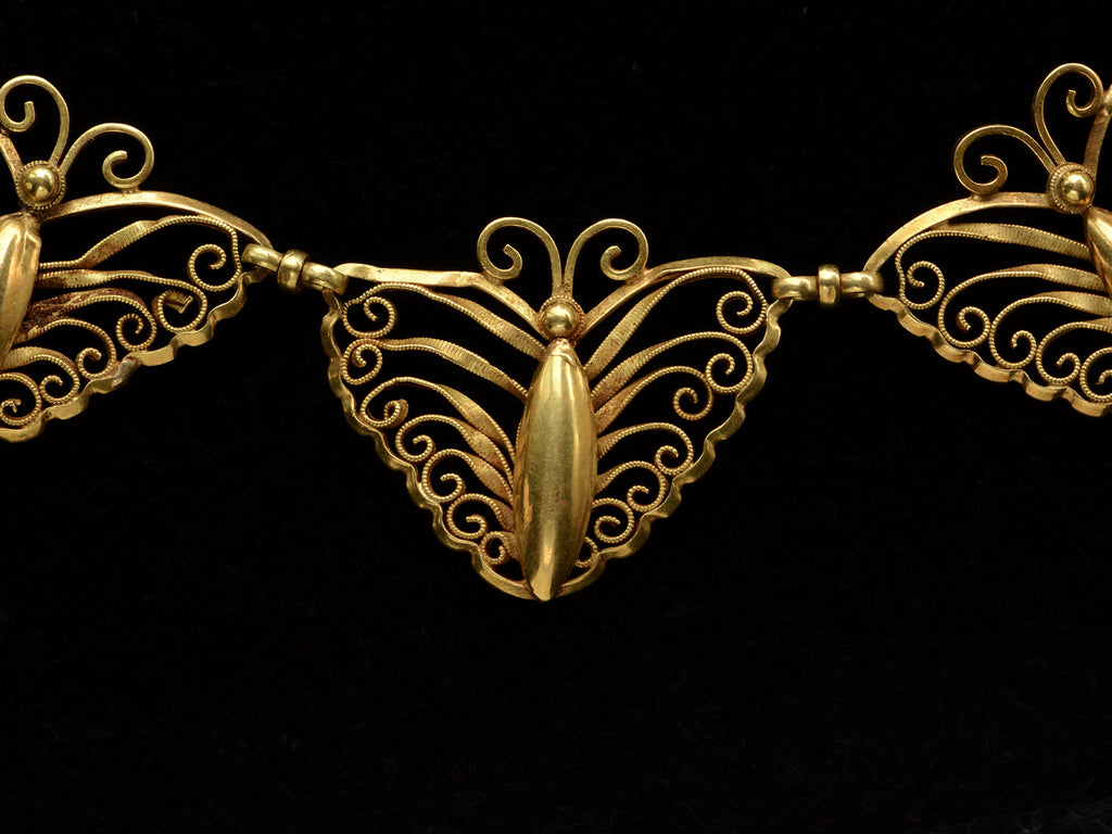 Closer up detail of an antique French gold filigree necklace featuring three large butterfly motifs at the front, shown on black background.