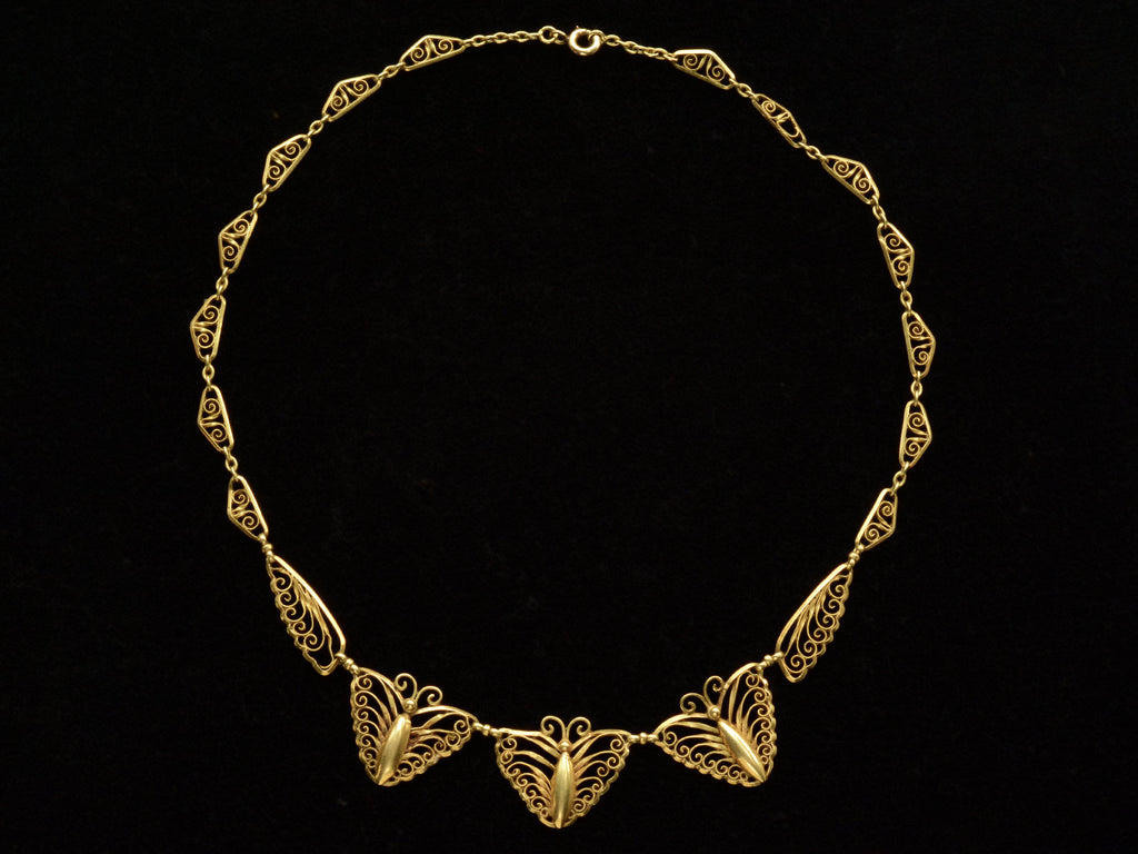 Am antique French gold filigree chain necklace with three butterfly-shaped pendants at the front, displayed against a solid black background.