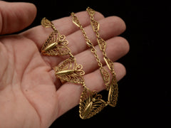 thumbnail of An antique gold filigree chain necklace with three large decorative leaf-like pendants, held in a person's hand against a black background.
