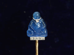 thumbnail of Detail of French stick pin with blue glass Buddha decorated with diamonds in platinum and yellow gold, shown on dark background.