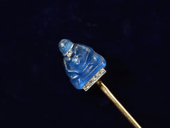thumbnail of Angled detail view of French stick pin with blue glass Buddha decorated with diamonds in platinum and yellow gold, shown on dark background.