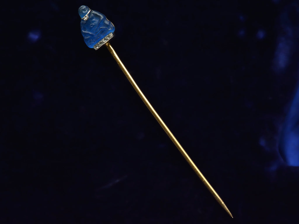 French stick pin with blue glass Buddha decorated with diamonds in platinum and yellow gold, shown on dark background.