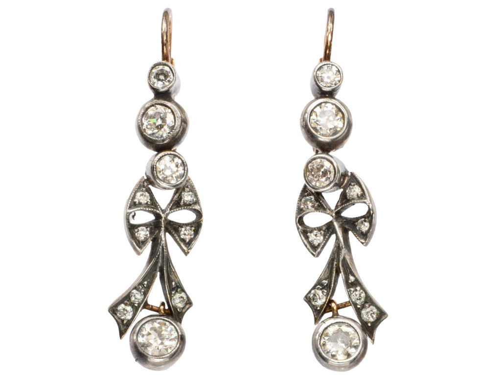 A pair of c1890 Victorian drop earrings with old European cut diamonds set in silver topped gold with a bow design. Shown on white background.