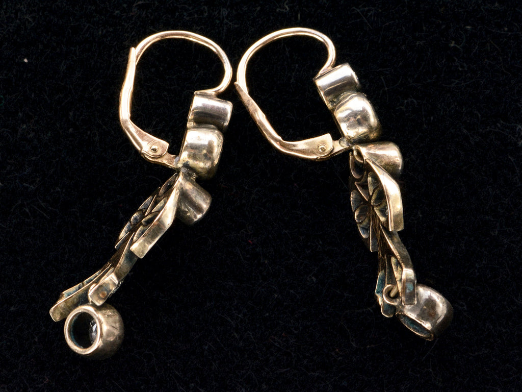 Alternate side view of a pair of c1890 Victorian drop earrings with old European cut diamonds set in silver topped gold with a bow design. Shown on black background.