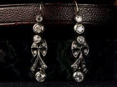 thumbnail of A pair of c1890 Victorian drop earrings with old European cut diamonds set in silver topped gold with a bow design. Shown on black background.