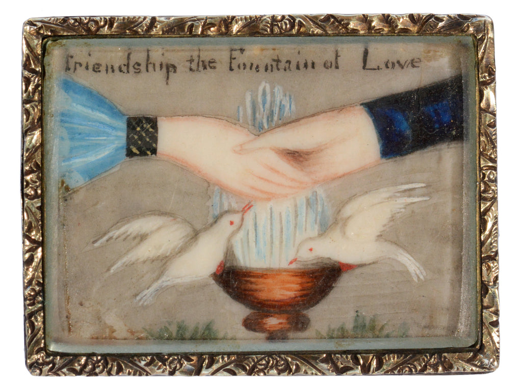 An antique Georgian-era rectangular brooch with hands and doves and the words "Friendship the Fountain of Love" with a gold frame. Shown on white background.