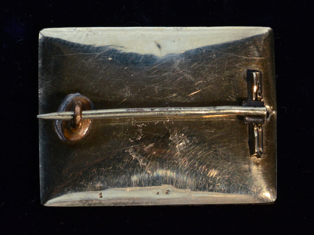 The reverse side of an antique Georgian-era rectangular brooch. Shown on black background.