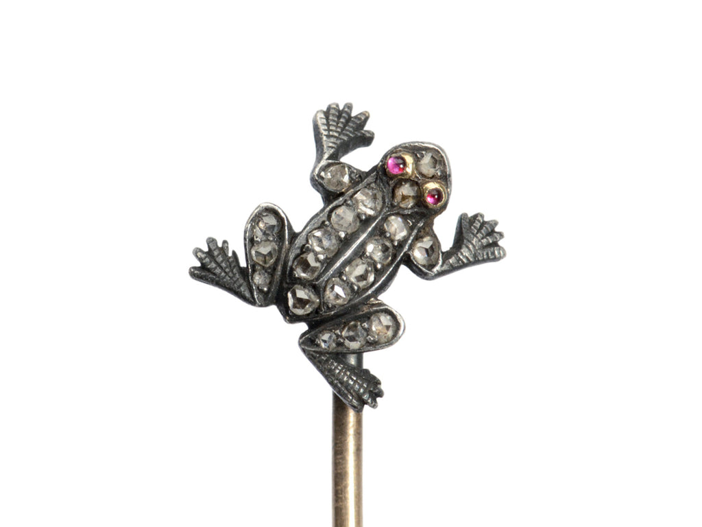 Detail of antique frog stick pin in silver and gold with rose cut diamonds and ruby eyes, shown on white background.