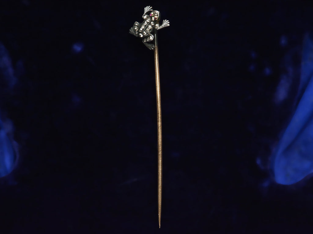 Antique frog stick pin in silver and gold with rose cut diamonds and ruby eyes, shown on dark background.