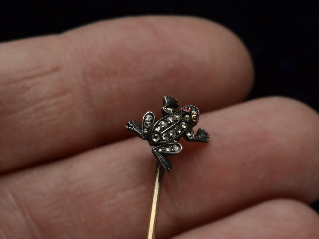 Detail of antique frog stick pin in silver and gold with rose cut diamonds and ruby eyes, shown on hand.
