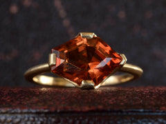 thumbnail of Front view of shield shaped orangey red stone set in 18K yellow gold, on dark background.