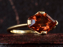 thumbnail of Left, angled view of shield shaped orangey red stone set in 18K yellow gold, on dark background.