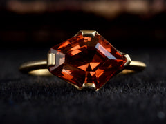 thumbnail of Face on view of shield shaped orangey red stone set in 18K yellow gold, on dark background.