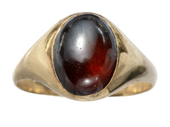 thumbnail of A domed antique yellow gold ring with a flush set oval dark red garnet cabochon. Shown on white background.