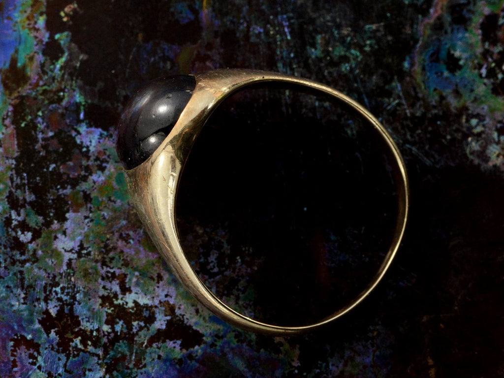 Side profile of a domed antique yellow gold ring with a flush set oval dark red garnet cabochon. Shown on dark background.