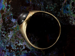 thumbnail of Side profile of a domed antique yellow gold ring with a flush set oval dark red garnet cabochon. Shown on dark background.