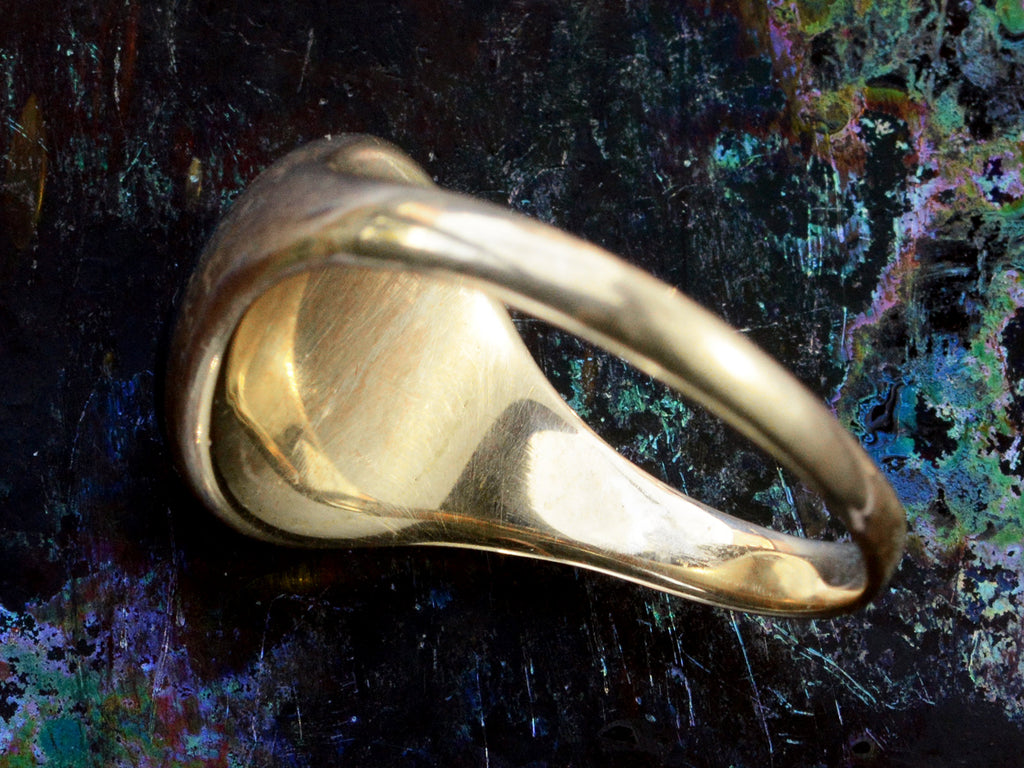 Underside/inside view of  domed antique yellow gold ring with a flush set oval dark red garnet cabochon. Shown on dark iridescent background.