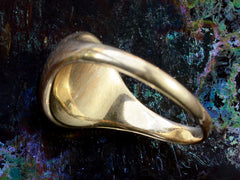 thumbnail of Underside/inside view of  domed antique yellow gold ring with a flush set oval dark red garnet cabochon. Shown on dark iridescent background.