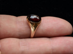 thumbnail of Side view of a domed antique yellow gold ring with a flush set oval dark red garnet cabochon. Shown on finger.