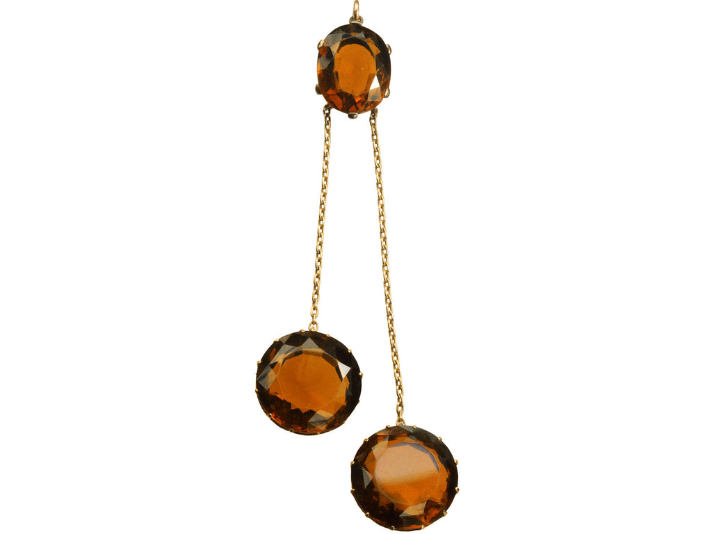 A massive gold Arts & Crafts movement pendant with an oval amber-colored garnet top and two large round amber-colored garnet drops. On white background.