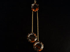 thumbnail of A massive gold Arts & Crafts movement pendant with an oval amber-colored garnet top and two large round amber-colored garnet drops. On black background.