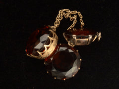 thumbnail of Detail of settings of a massive gold Arts & Crafts movement pendant with an oval amber-colored garnet top and two large round amber-colored garnet drops. On black background.