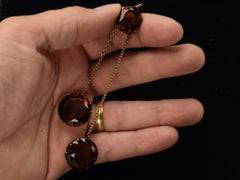 thumbnail of A massive gold Arts & Crafts movement pendant with an oval amber-colored garnet top and two large round amber-colored garnet drops. Held in hand.