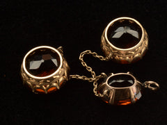 thumbnail of Detail of reverse side of settings of a massive gold Arts & Crafts movement pendant with an oval amber-colored garnet top and two large round amber-colored garnet drops. On black background.
