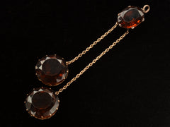 thumbnail of Angled view of a massive gold Arts & Crafts movement pendant with an oval amber-colored garnet top and two large round amber-colored garnet drops. On black background.