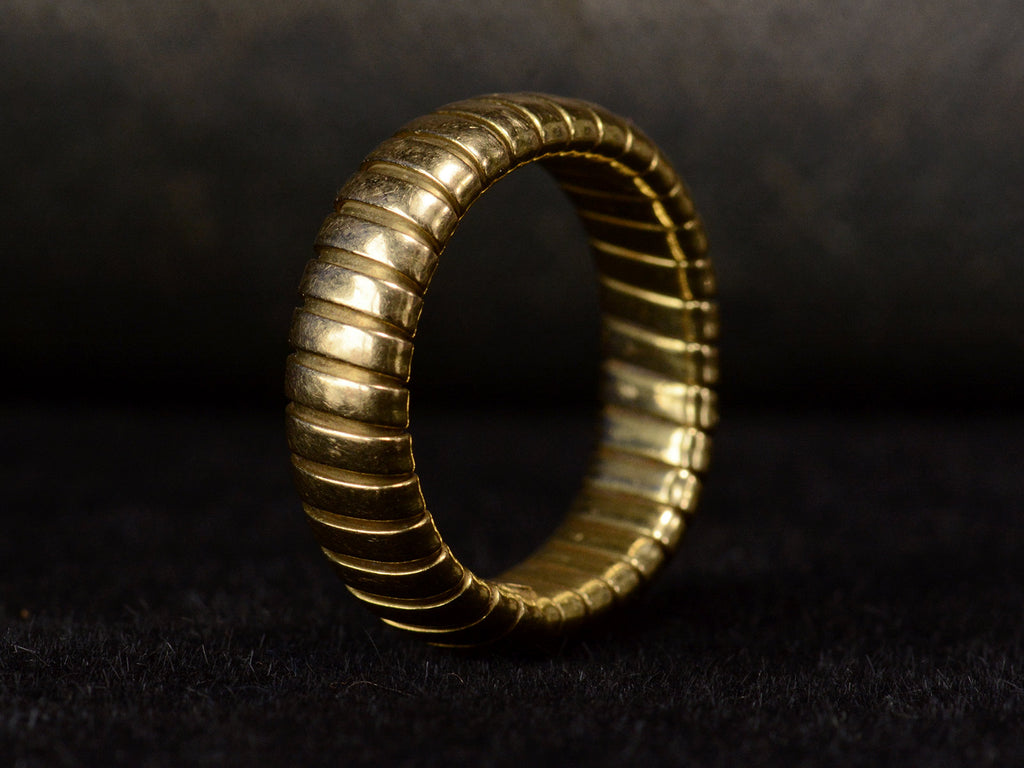 Angled view of flexible gaspipe-link 18k yellow gold band, shown on dark background.